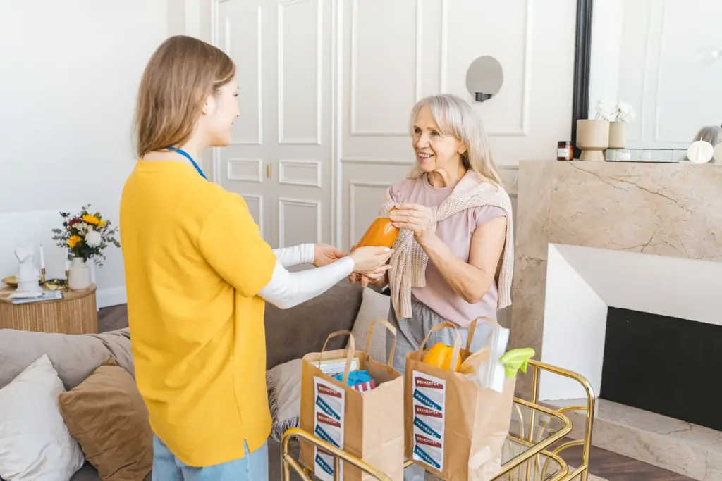 Helferin übergibt einer Seniorin die Einkäufe zu Hause