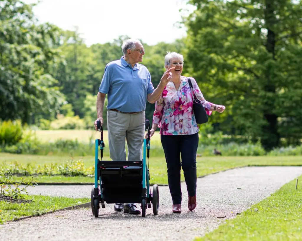 Frau und Mann mit Rollator gehen lachend gemeinsam durch einen Park
